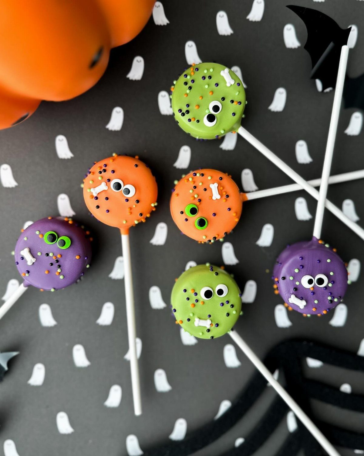 Halloween cake pops in green, orange, and purple with candy eyes and sprinkles.