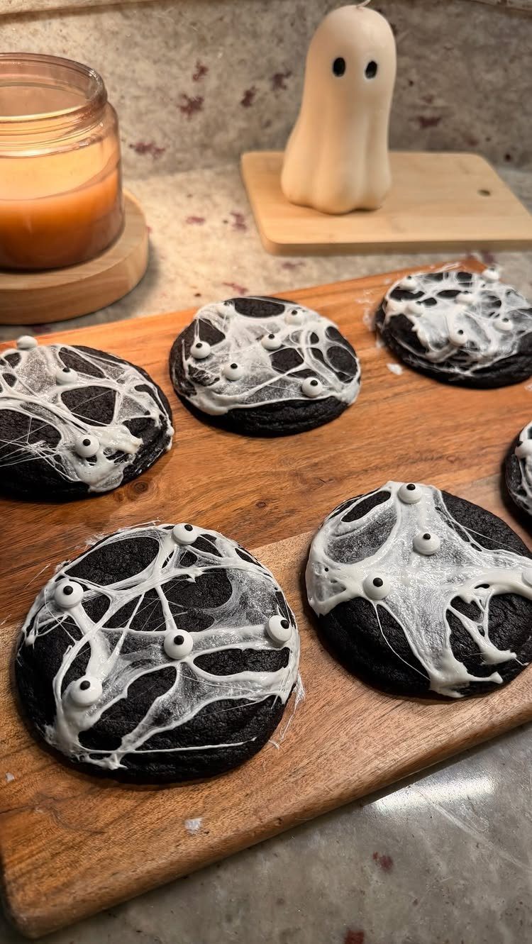 Black cookies with white spiderweb icing and candy eyeballs on a wooden board