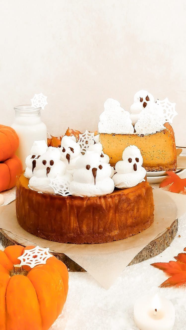 Pumpkin cheesecakes topped with whipped cream ghosts surrounded by pumpkins and autumn leaves