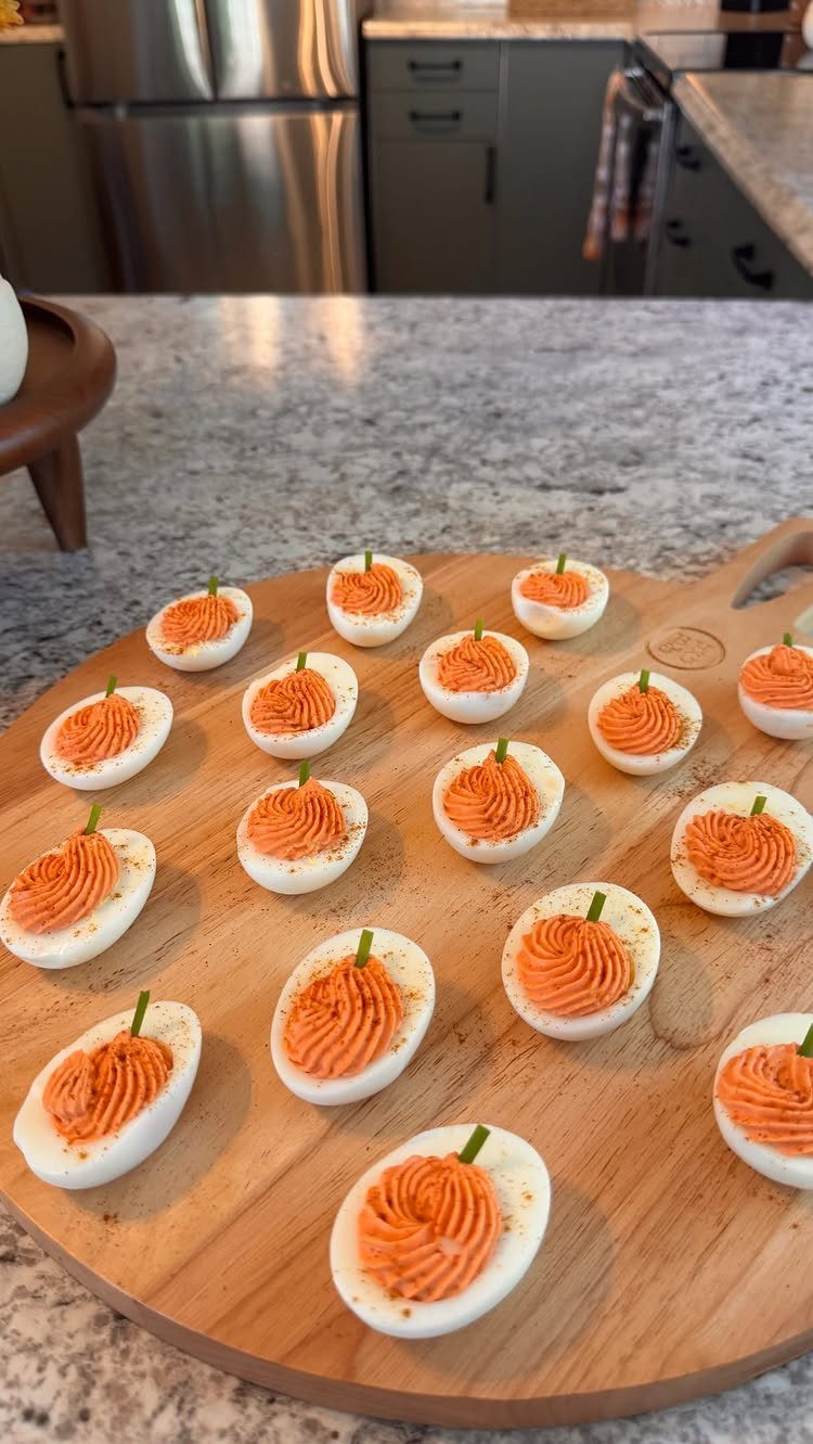 Pumpkin shaped deviled eggs with orange filling and green stems on wooden board