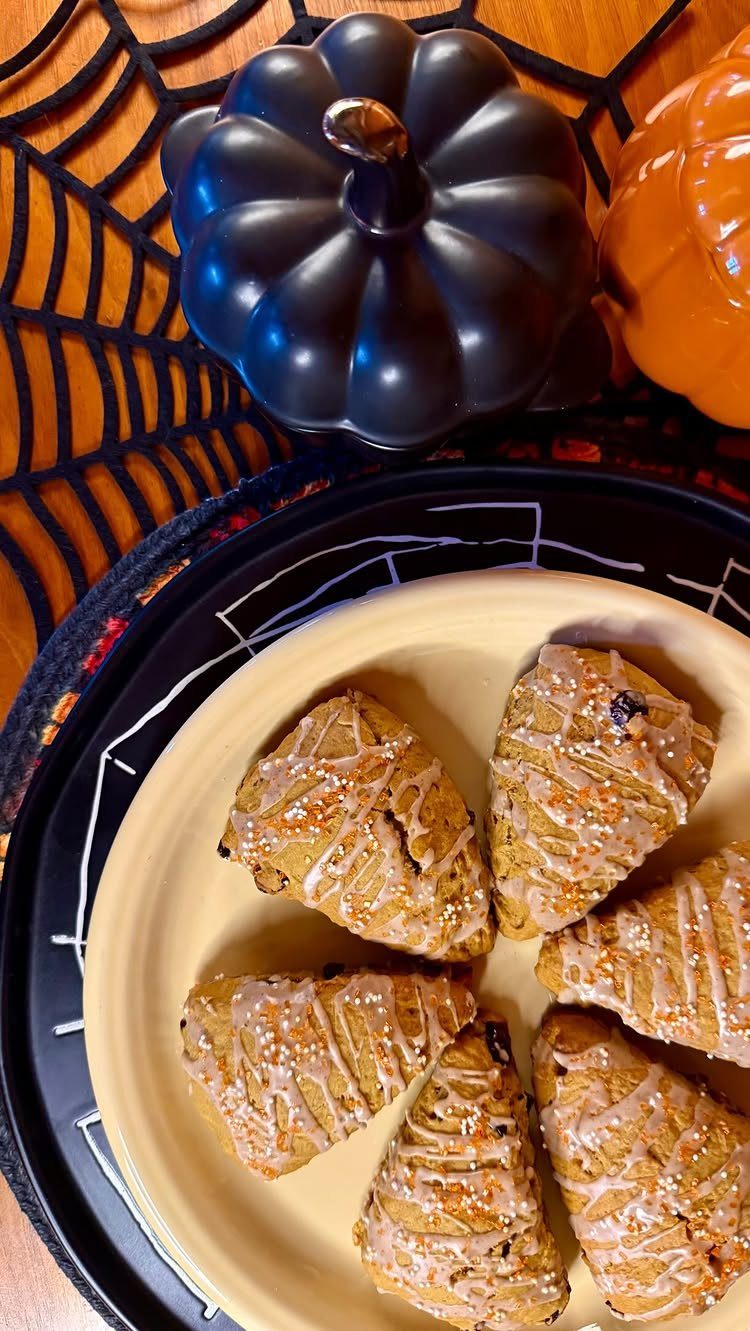 Glazed pumpkin scones on a plate with decorative pumpkins and spiderweb mat.