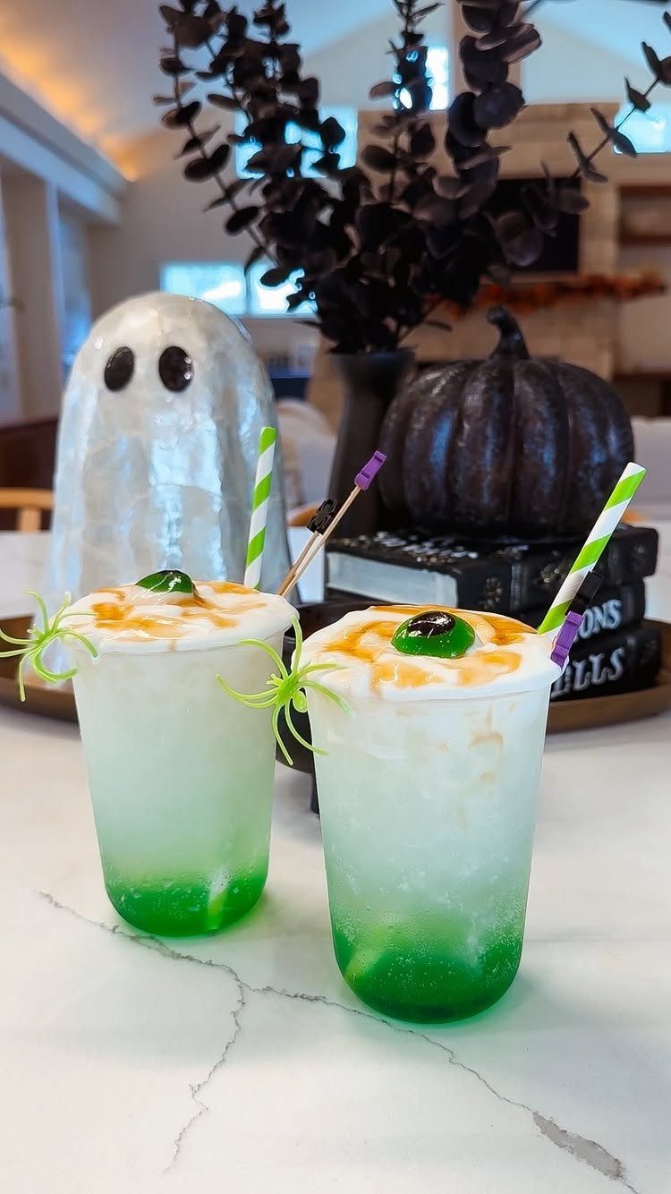 Two layered green and white Halloween cocktails topped with foam and plastic spiders.