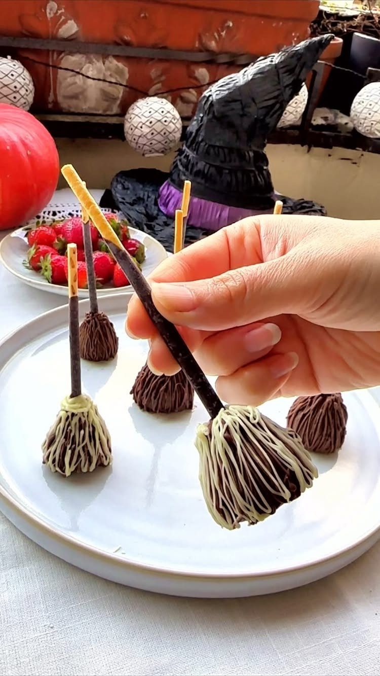Broom-shaped treats made of pretzel rods and chocolate truffles on a white plate.