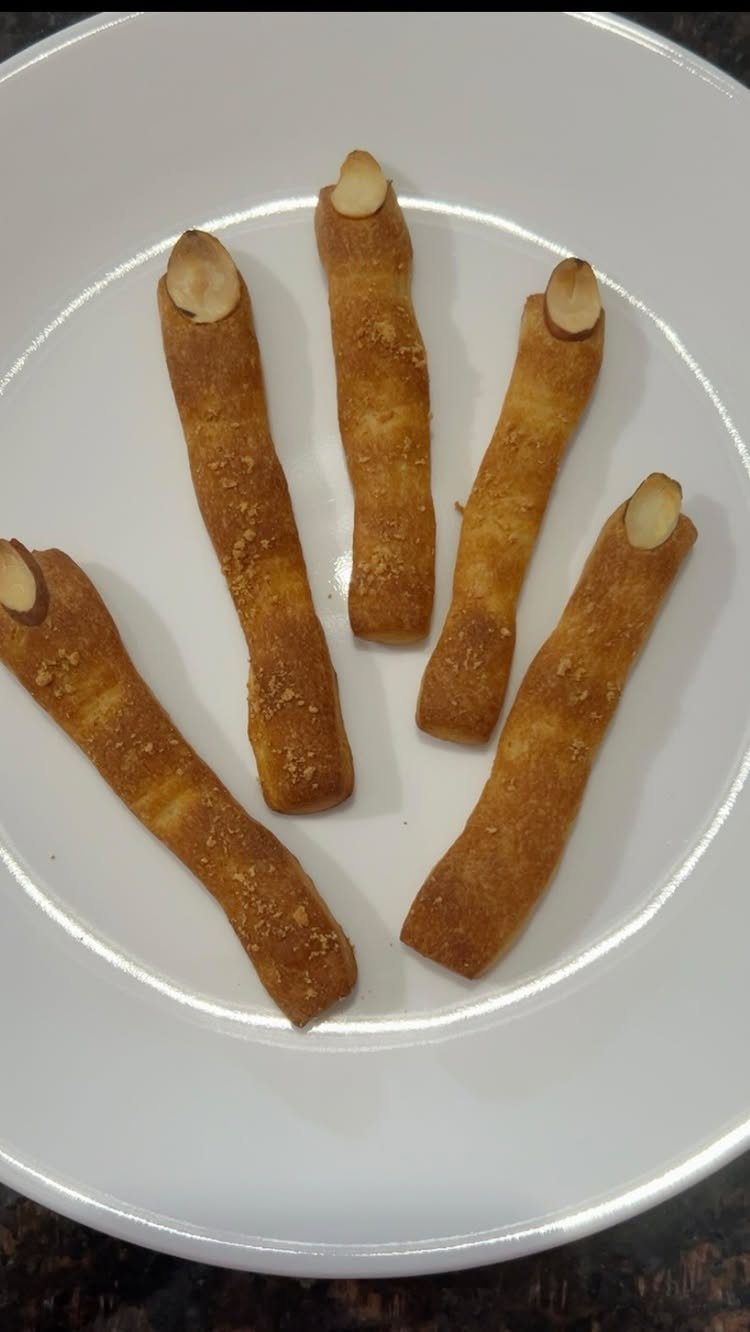 Breadsticks shaped like witch fingers with almond nails on a white plate.
