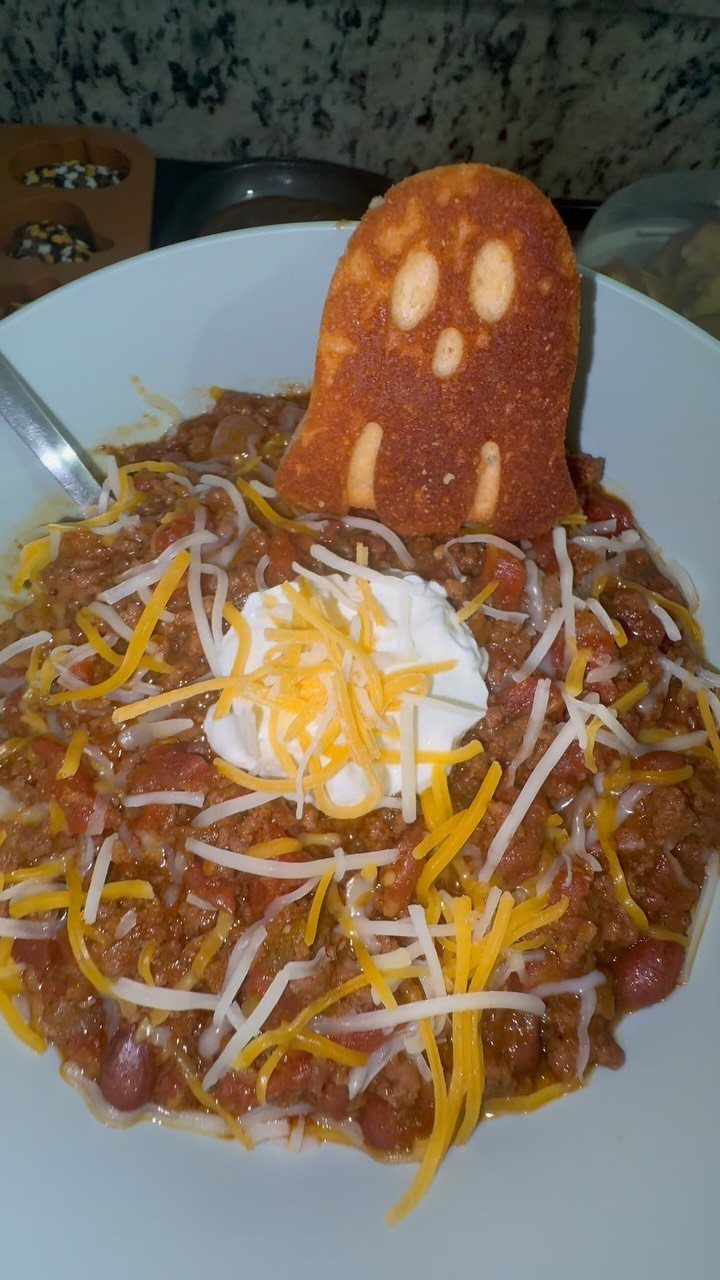 Bowl of chili topped with cheese and sour cream with a ghost-shaped toast.