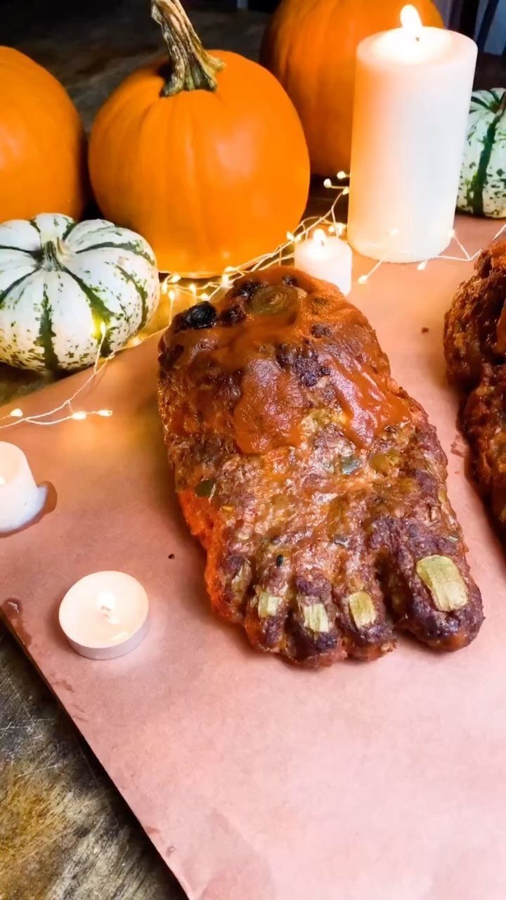 Meatloaf shaped like a foot with onion toenails surrounded by pumpkins and candles.