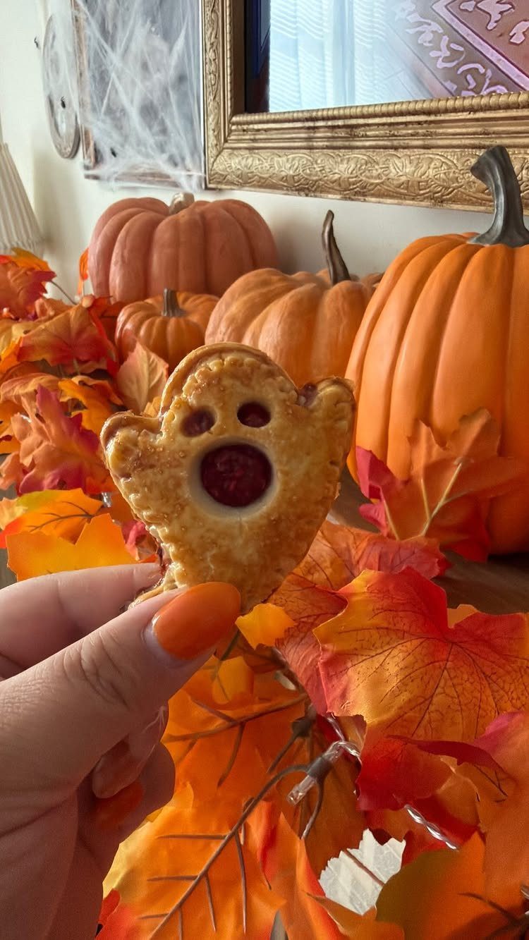 Ghost-shaped hand pie held against a background of pumpkins and autumn leaves.