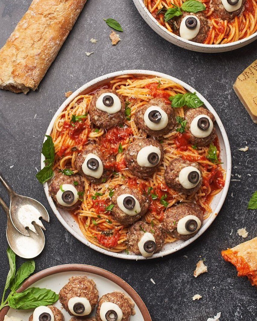 Spaghetti and meatballs with mozzarella and olive eyeballs served in a white bowl.
