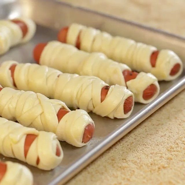 Mummy hot dogs wrapped in dough strips on a metal baking sheet.