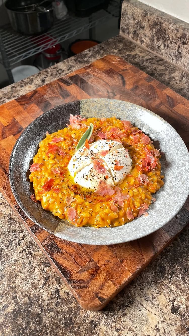 Orange pumpkin risotto topped with a poached egg and prosciutto in a grey bowl.