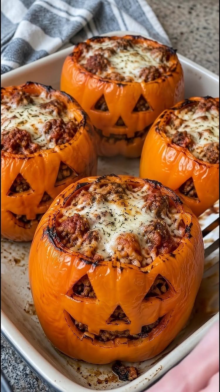 Carved orange bell peppers filled with meat and cheese in a baking dish.