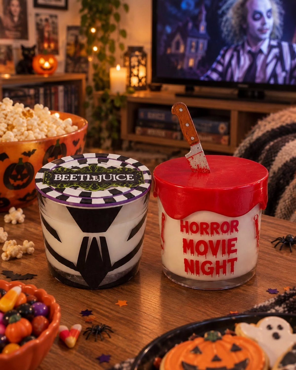 Themed Halloween candles on a table with popcorn and a movie playing behind.