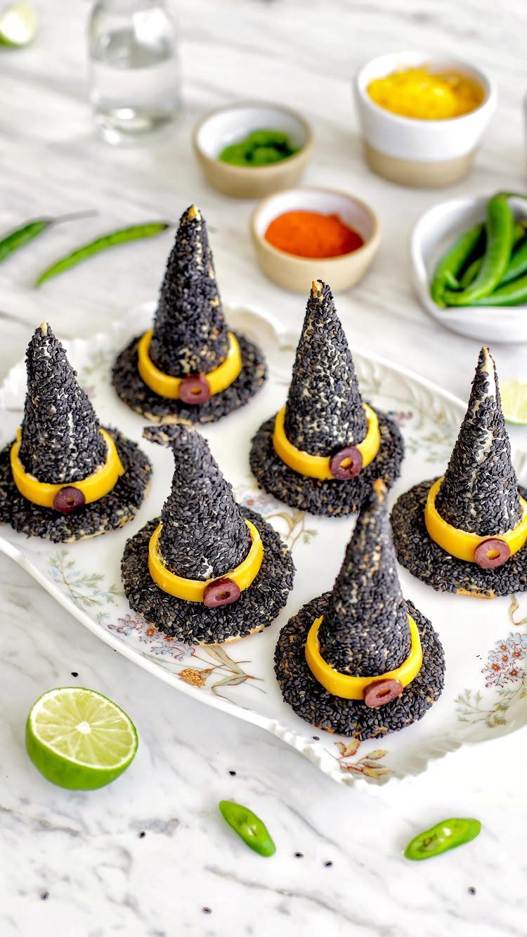 Witch hat appetizers coated in black sesame seeds on a floral white platter.