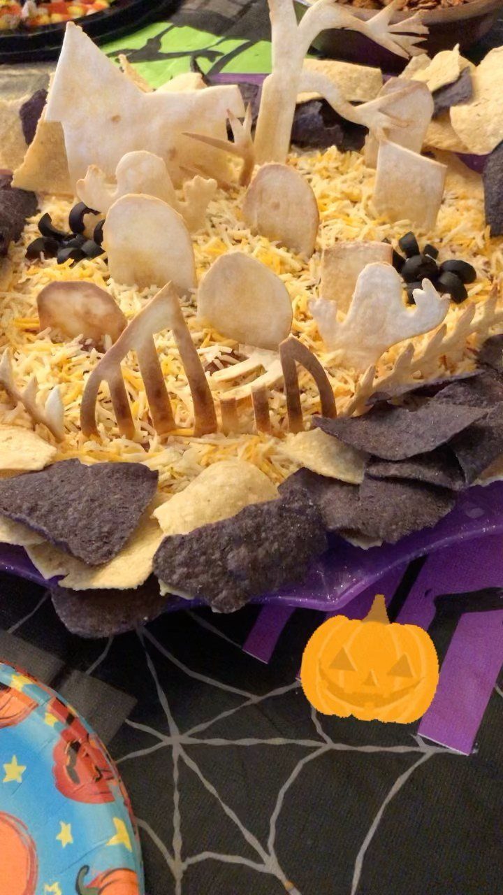 Graveyard dip with shredded cheese and tortilla chip tombstones on a purple platter.