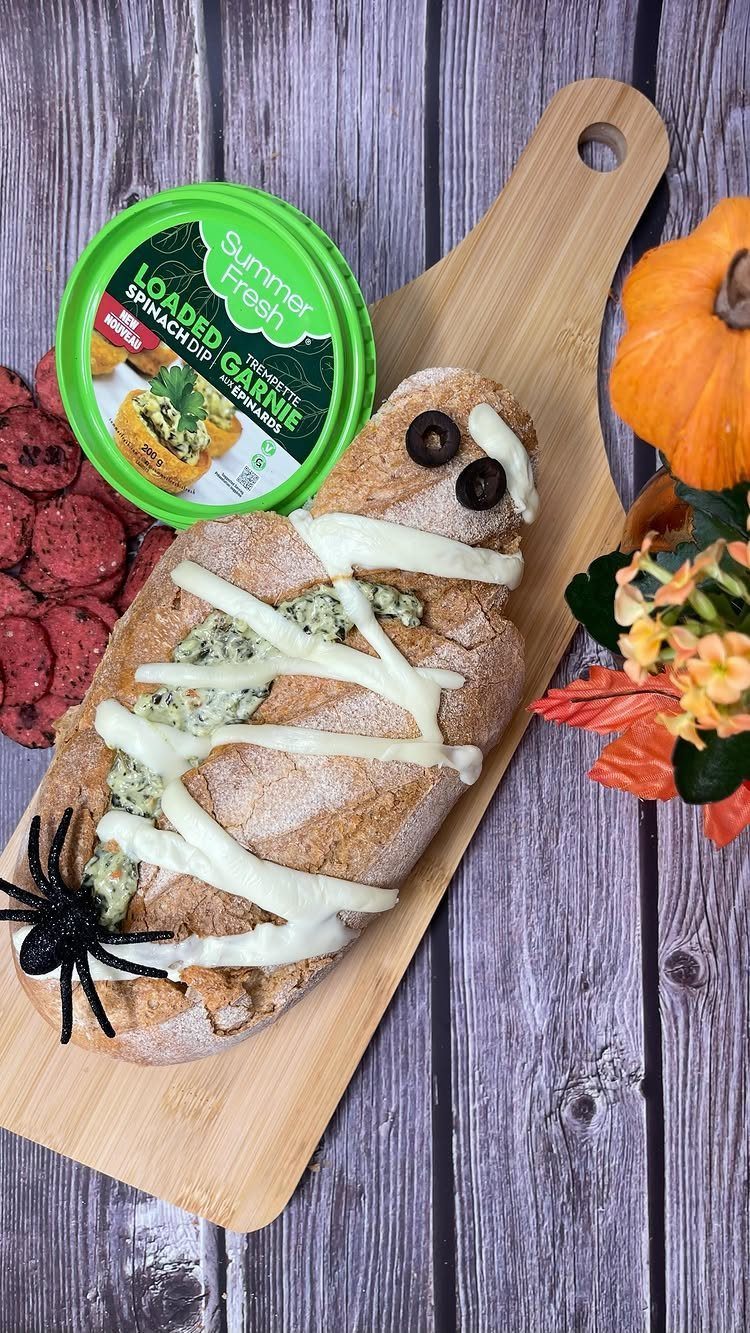 Mummy-shaped bread filled with spinach dip on a wooden board with a spider.