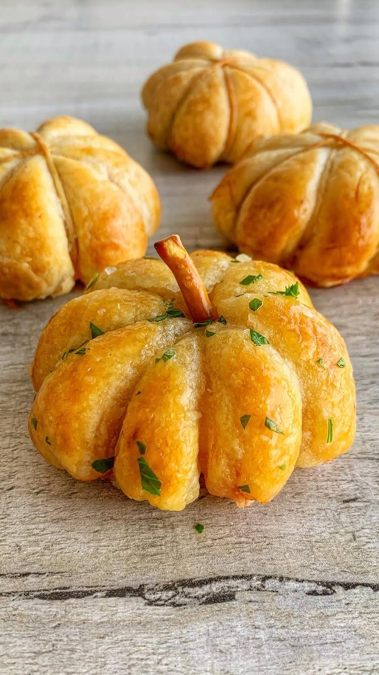 Pumpkin-shaped bread rolls with parsley garnish on a light wooden background.