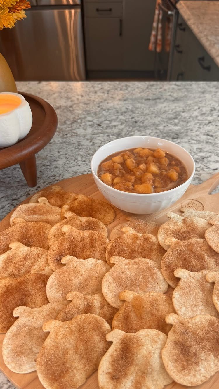Pumpkin-shaped cinnamon tortilla chips on a wooden board with a bowl of dip.