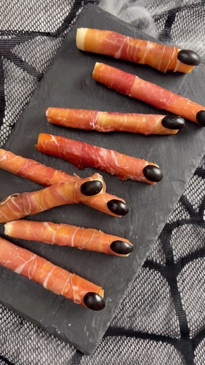 Finger-shaped meat appetizers with black olive nails on a black slate platter.