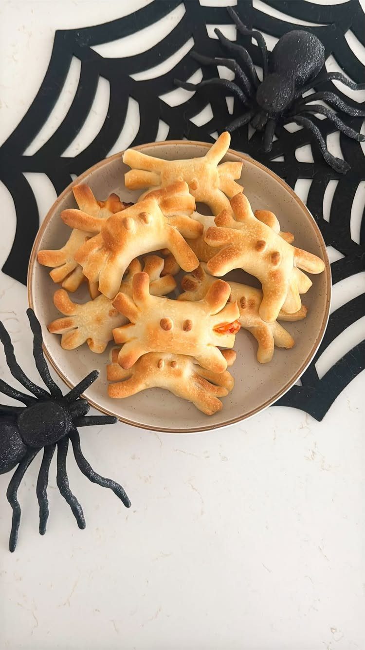 Spider-shaped bread rolls on a plate with black plastic spiders and web mat.