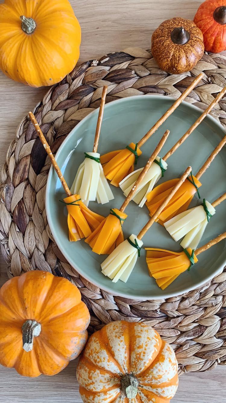 Cheese and carrot broomsticks on a blue plate surrounded by small orange pumpkins.
