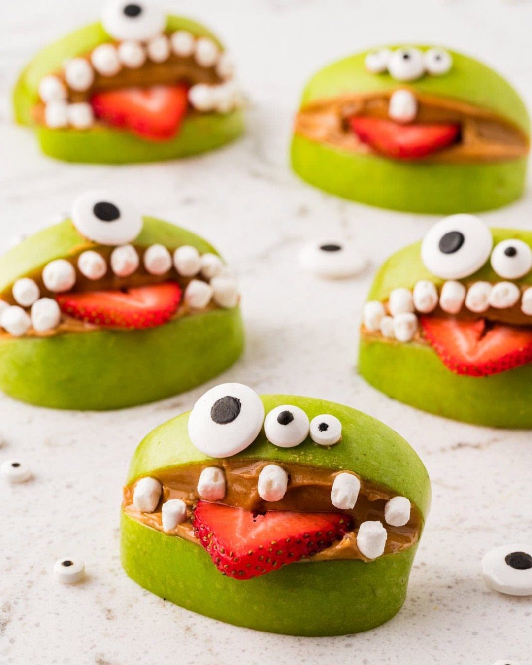 Green apple monster snacks with peanut butter, strawberry tongues, and candy eyes.