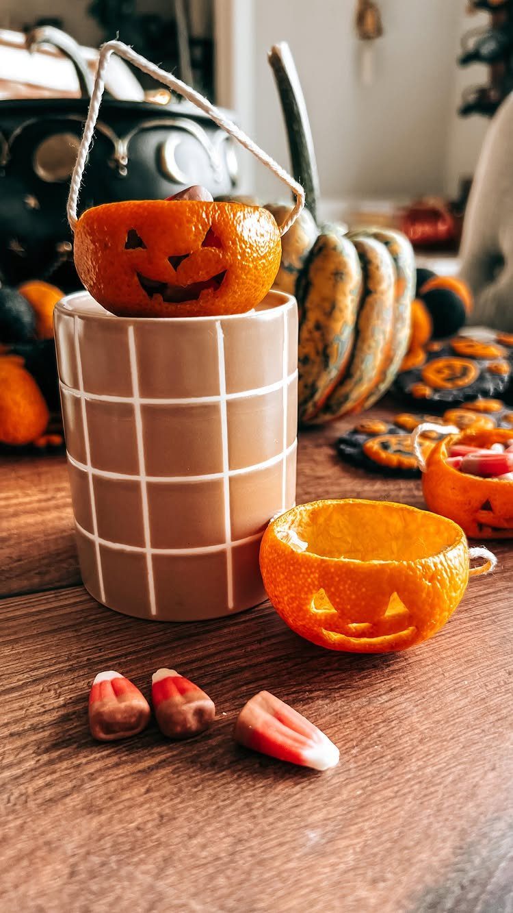 Clementines carved like jack-o'-lanterns on a wooden table with Halloween decorations.