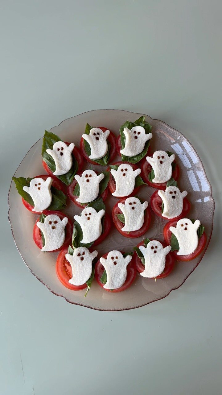 Mozzarella cheese ghosts on tomato slices with basil on a pink plate