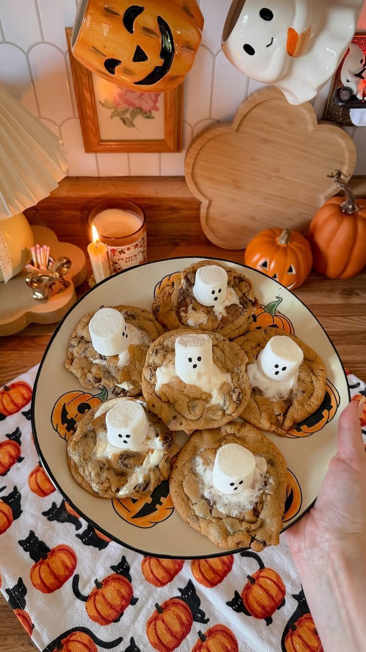 Chocolate chip cookies topped with marshmallow ghosts on a pumpkin-themed table setting.
