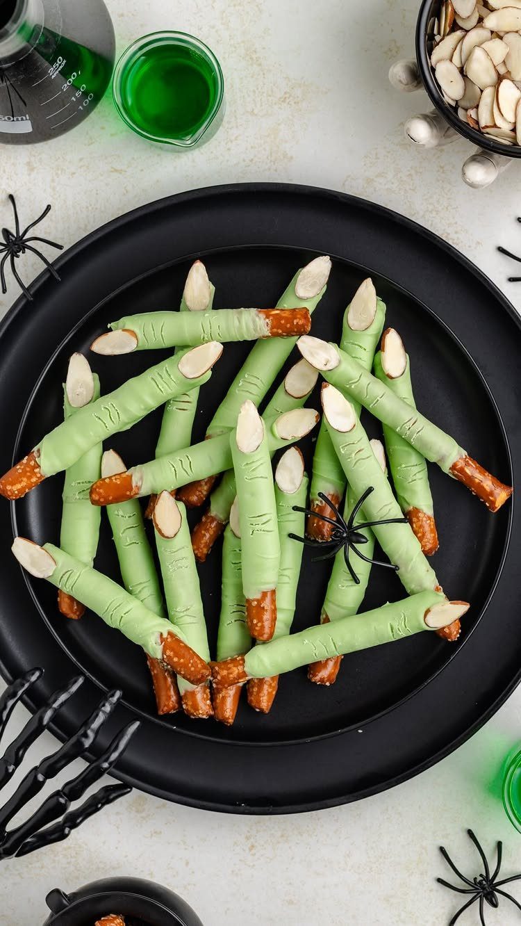 Green pretzel fingers with almond nails on a black plate with spooky decorations.