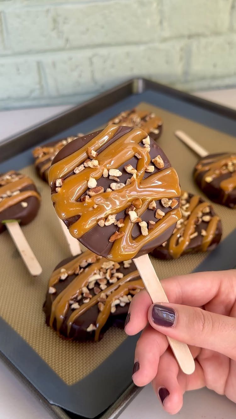 Chocolate covered apple slices drizzled with caramel and nuts on wooden sticks.