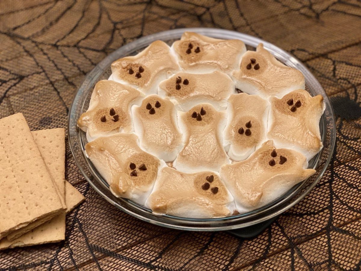 Toasted marshmallow ghosts in a glass dish with graham crackers on spiderweb lace.