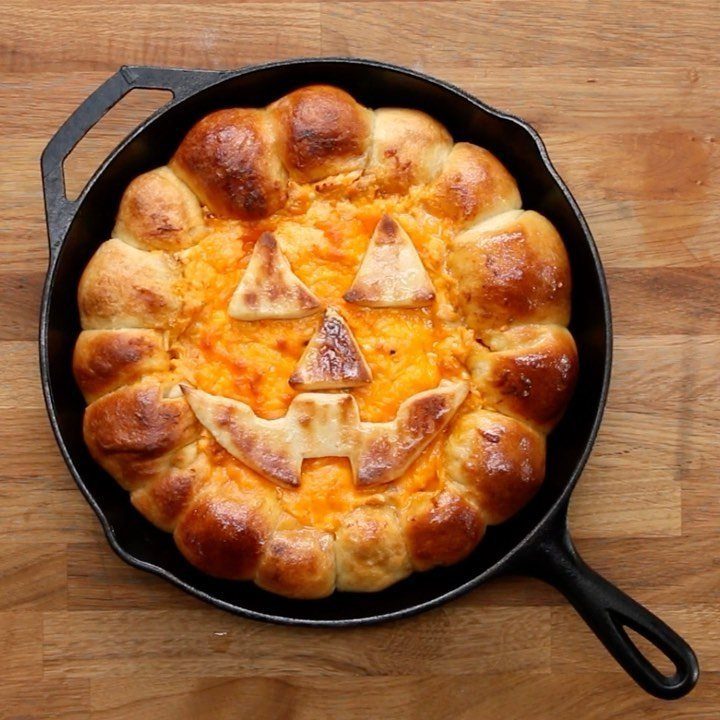 Cheesy orange dip in a skillet with a bread crust and pumpkin face.