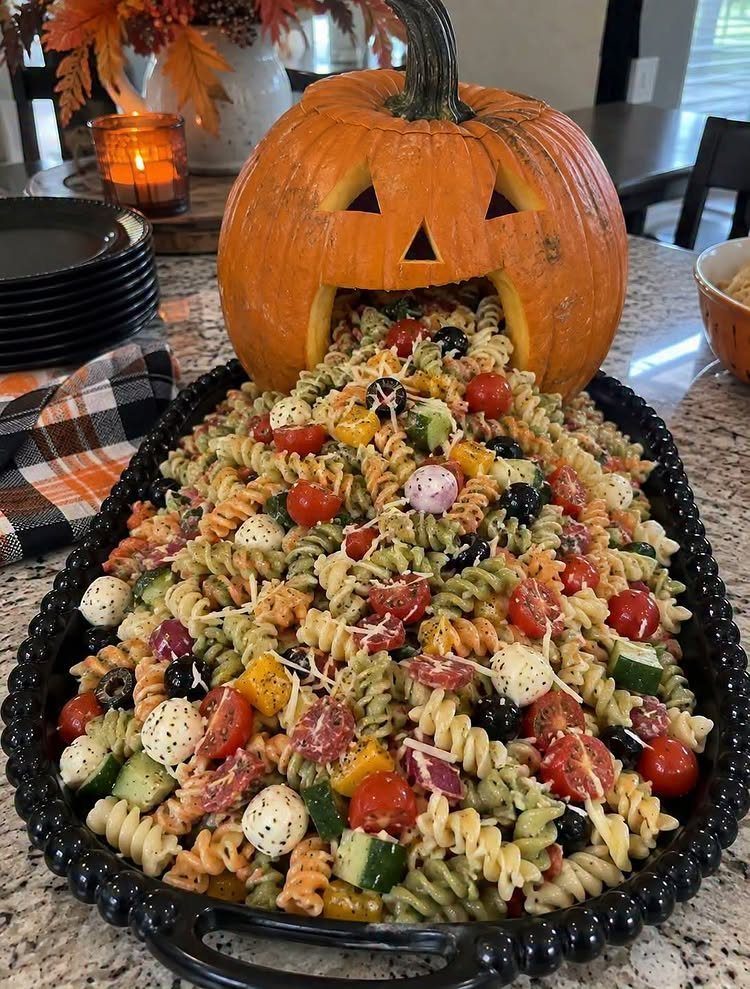 Carved pumpkin spilling colorful pasta salad onto a black serving platter