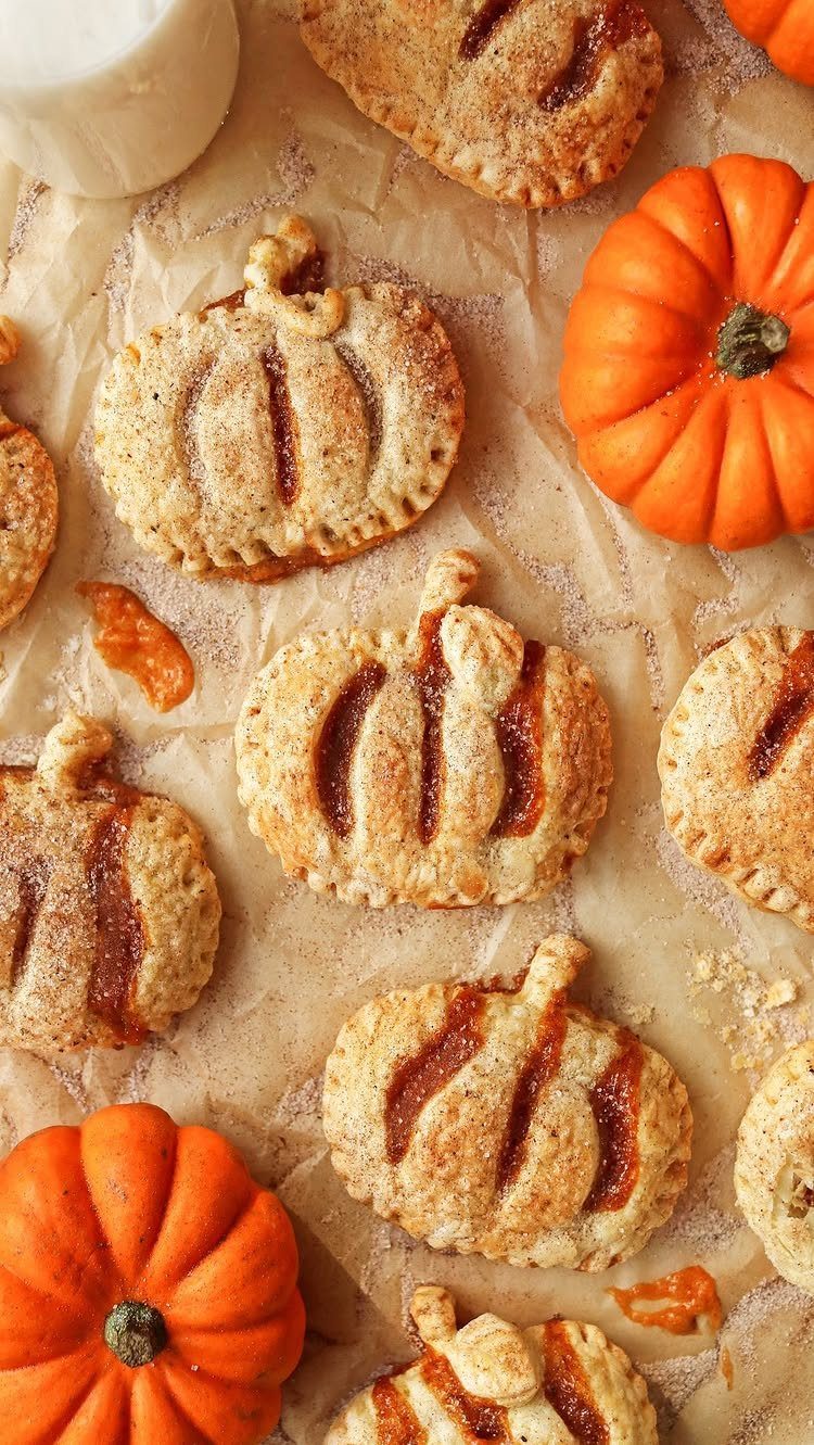 Pumpkin-shaped hand pies with orange filling on parchment paper with small pumpkins.