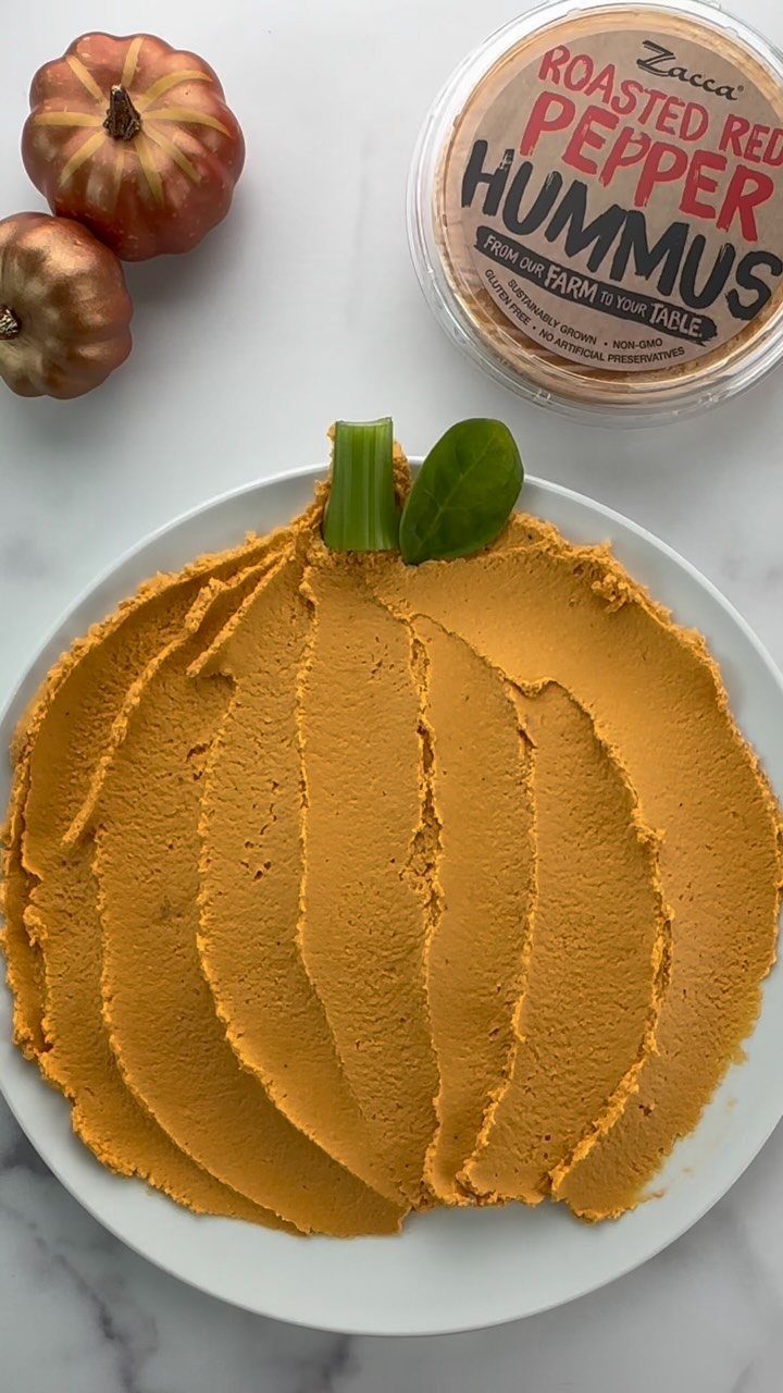 Orange hummus shaped like a pumpkin on a white plate with celery stem.