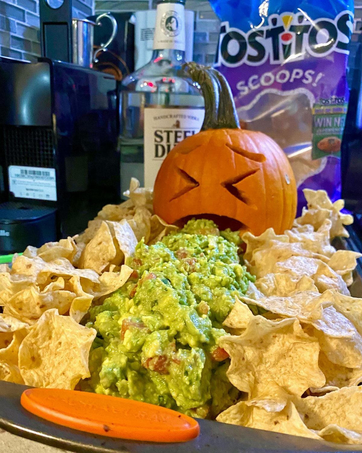 Guacamole spilling from a carved pumpkin mouth surrounded by tortilla chips