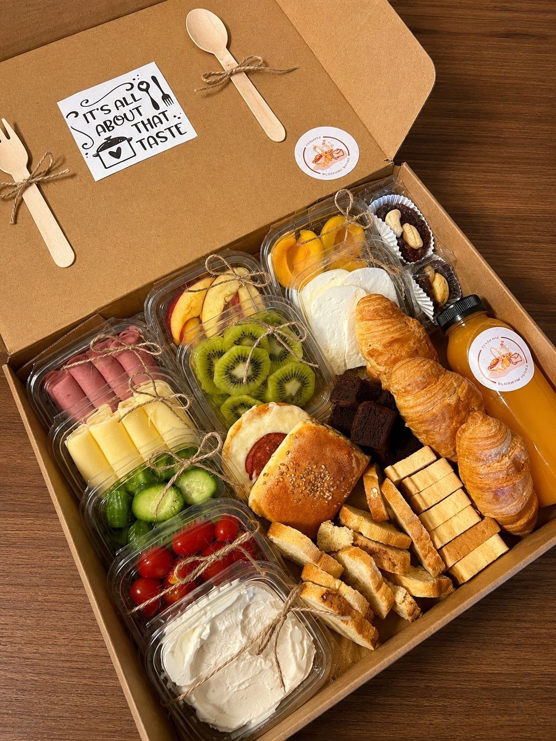 Breakfast box with croissants, fresh fruit, cheese, vegetables, and orange juice.