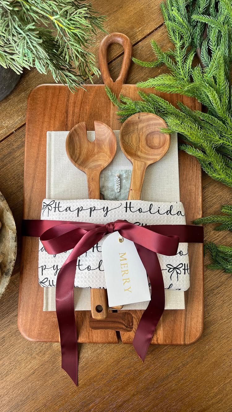 Wooden cutting board gift set with salad servers, red ribbon, and pine branches.