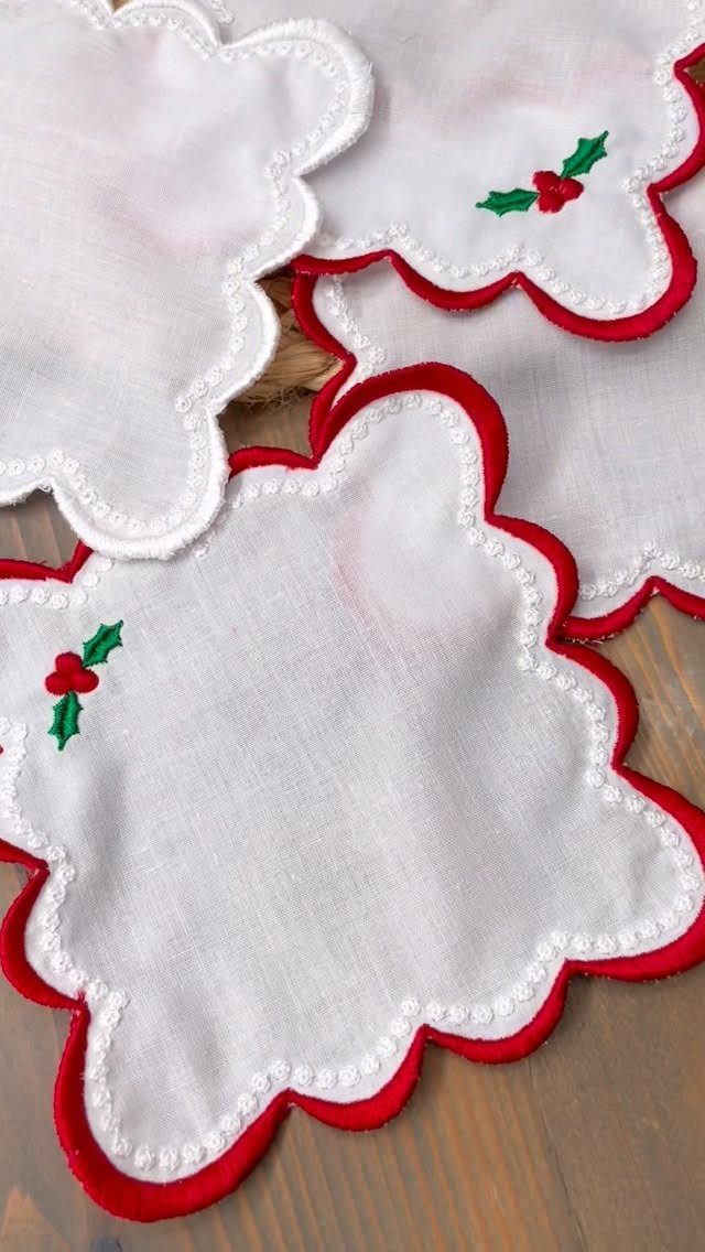 White scalloped fabric coasters with red trim and embroidered holly on wood.