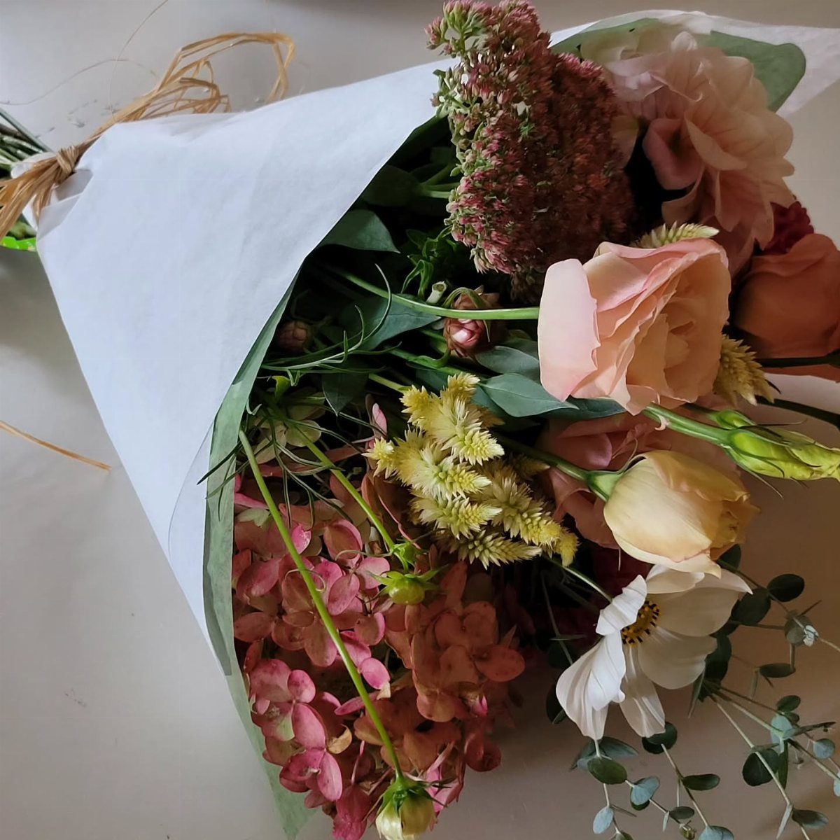 Bouquet of pink and peach flowers wrapped in white paper with twine.
