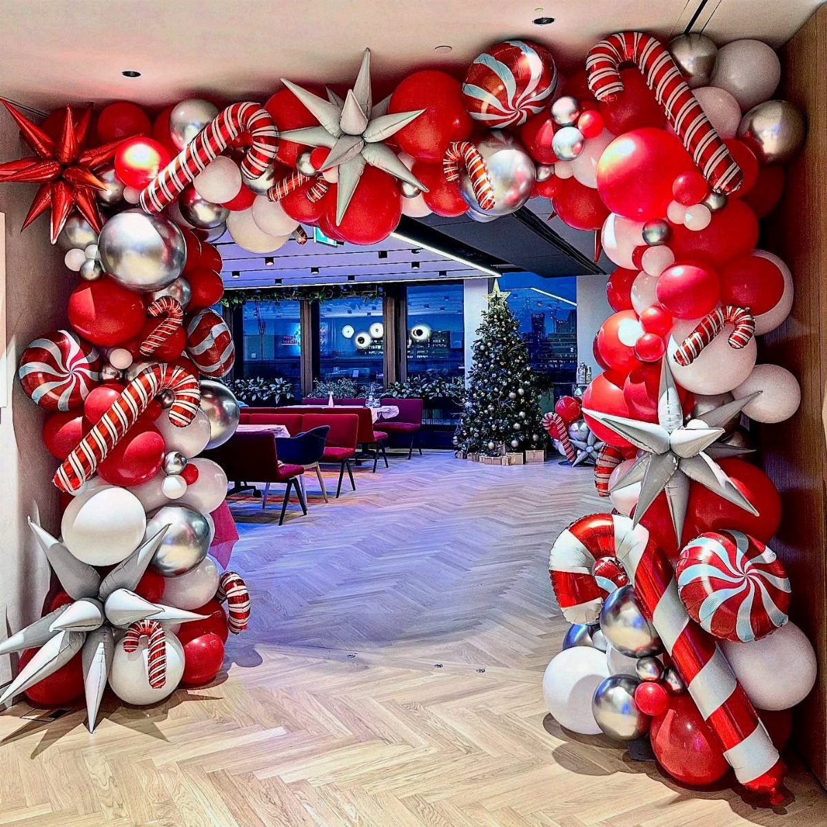 Festive red and white balloon arch with candy canes framing a Christmas party room.
