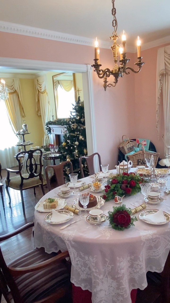 Festive tea table set with lace cloth, tea cups, cakes, and red roses.