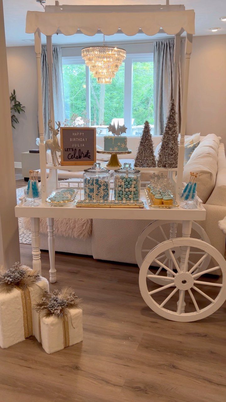 White candy cart with blue treats and glittery trees for a holiday party.