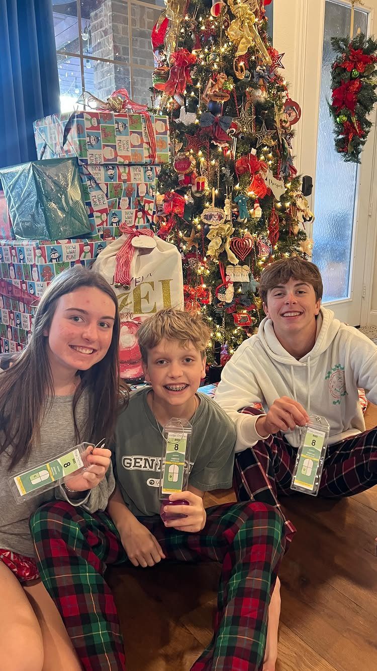 Three teenagers in pajamas sitting by a Christmas tree holding small gift prizes.