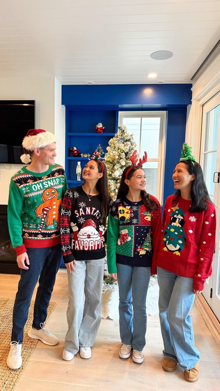 Four people wearing colorful ugly Christmas sweaters posing in a decorated living room.