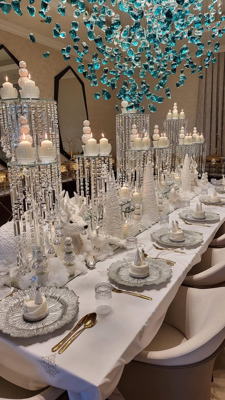 Elegant white dining table with crystal candle holders, faux snow, and blue chandelier.