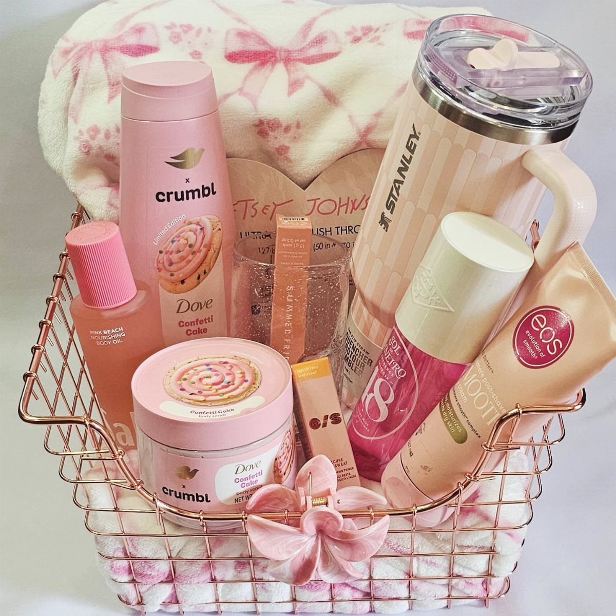 Rose gold wire basket filled with pink toiletries and a plush pink blanket.