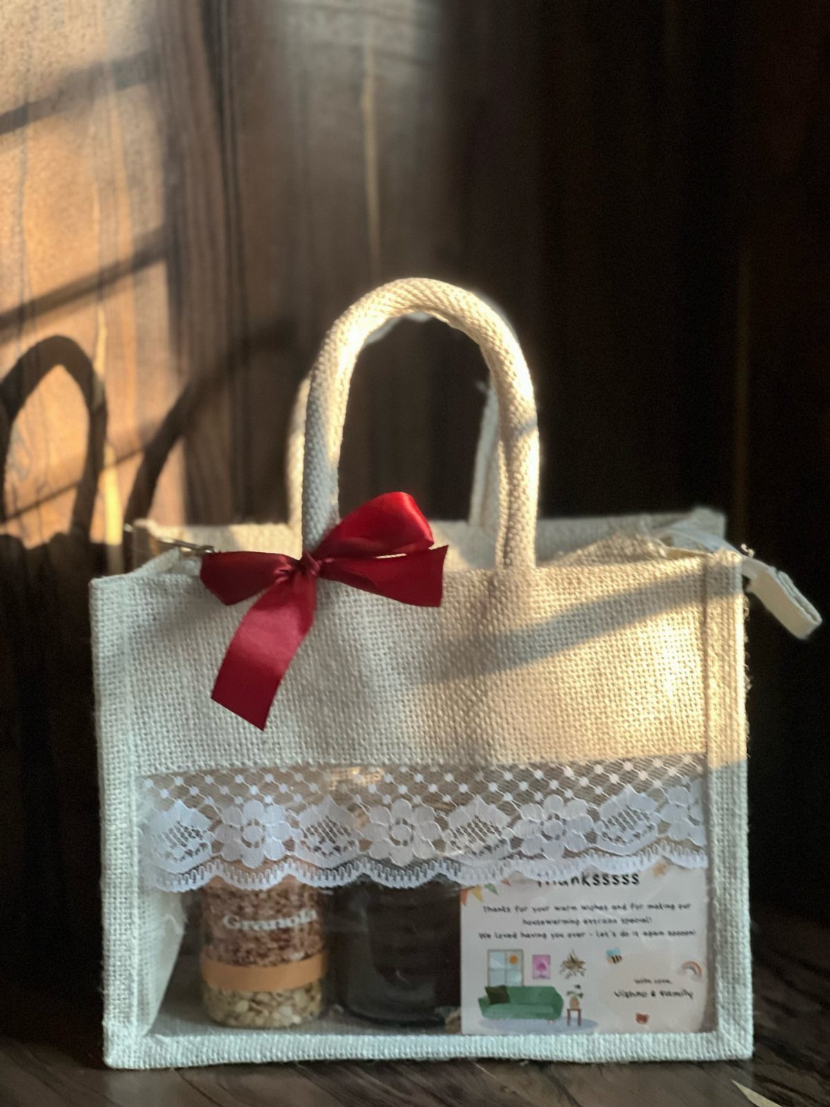 Burlap gift bag with red bow containing jars and a thank you note.