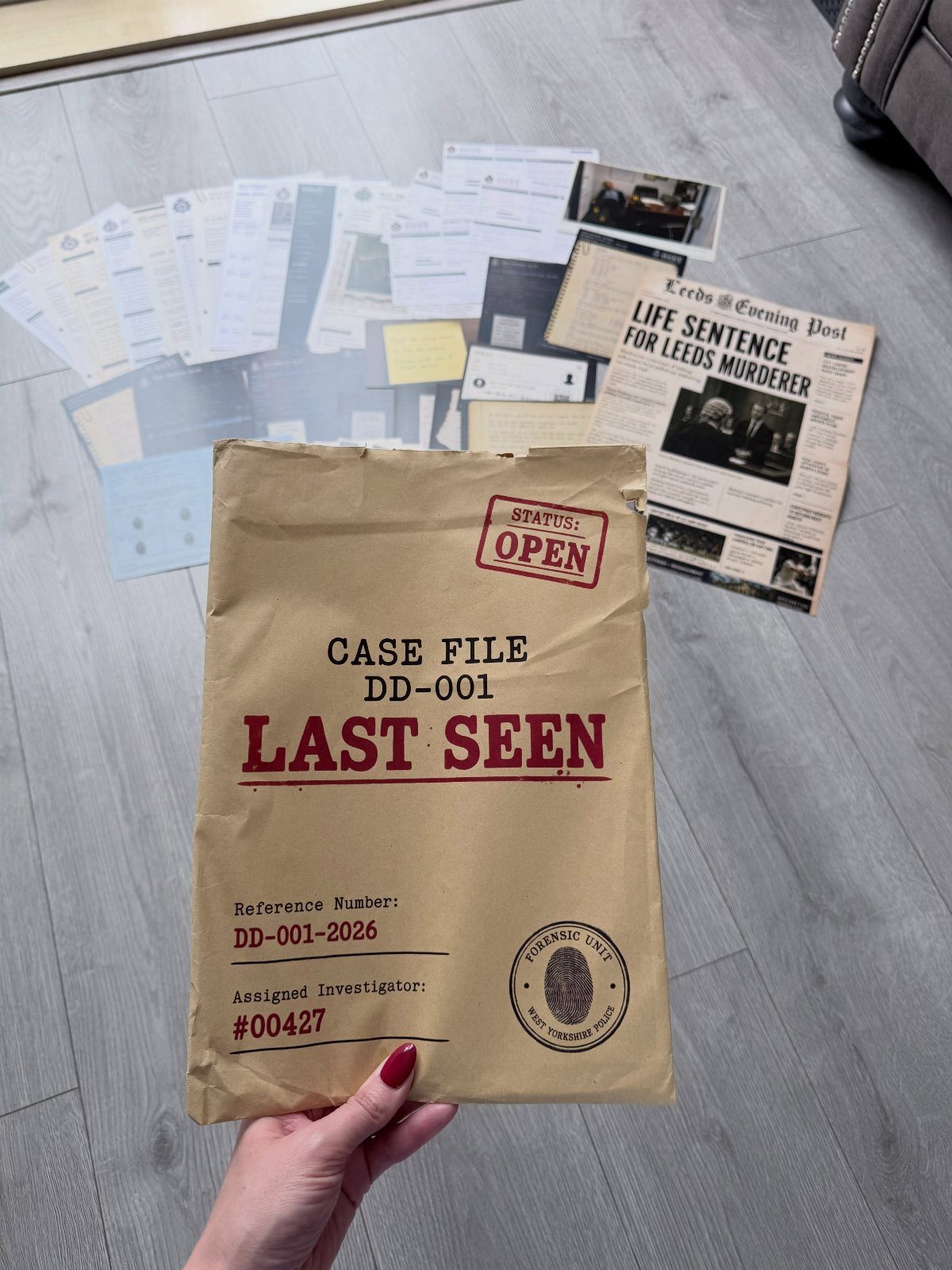 Brown case file envelope and crime scene documents spread on a grey floor.
