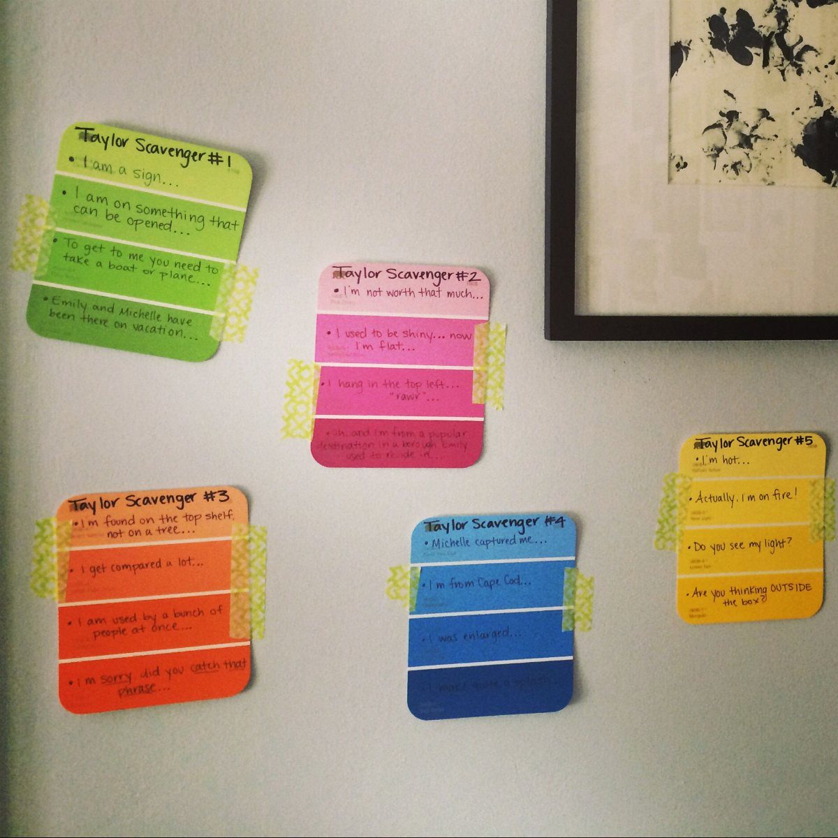 Colorful handwritten scavenger hunt clue cards taped to a plain white wall.